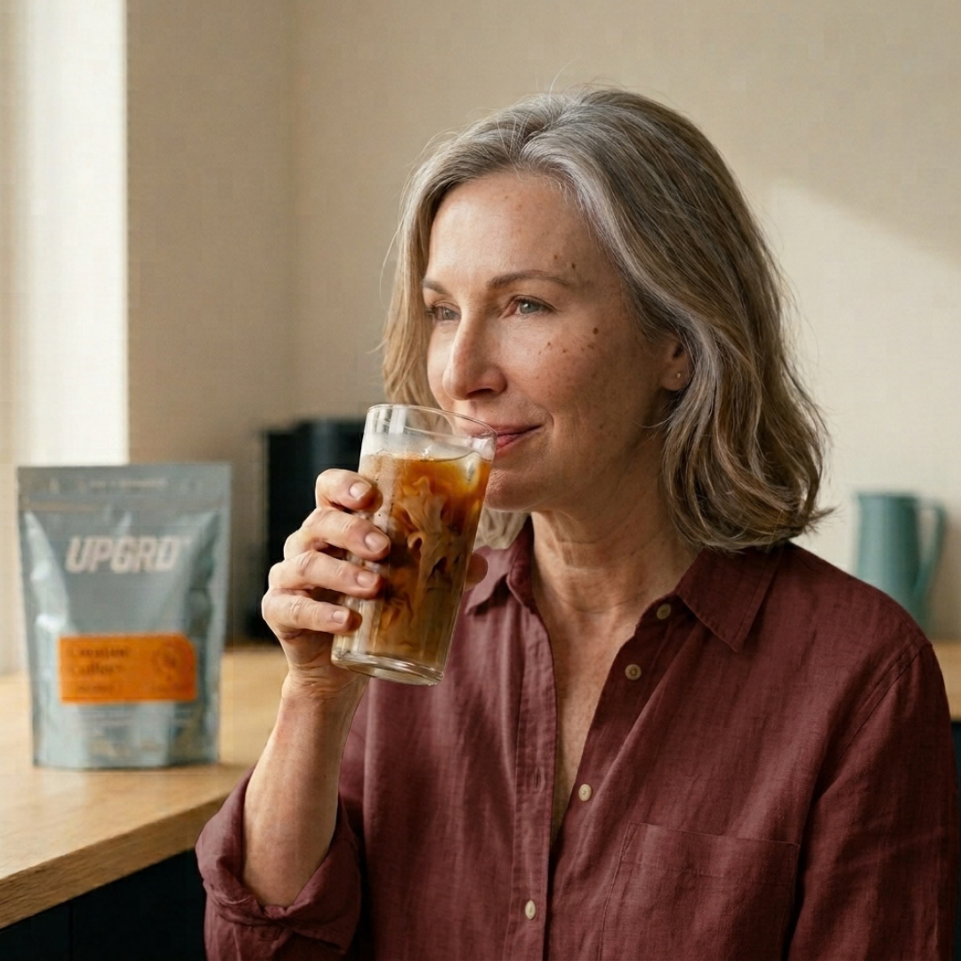 Woman drinking UPGRD creatine coffee over ice at her kitchen table